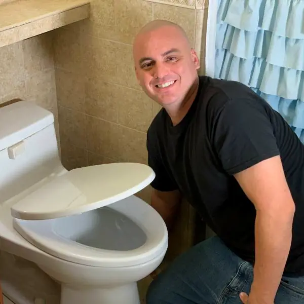 Danny kneeling beside a newly set toilet in a finished bathroom