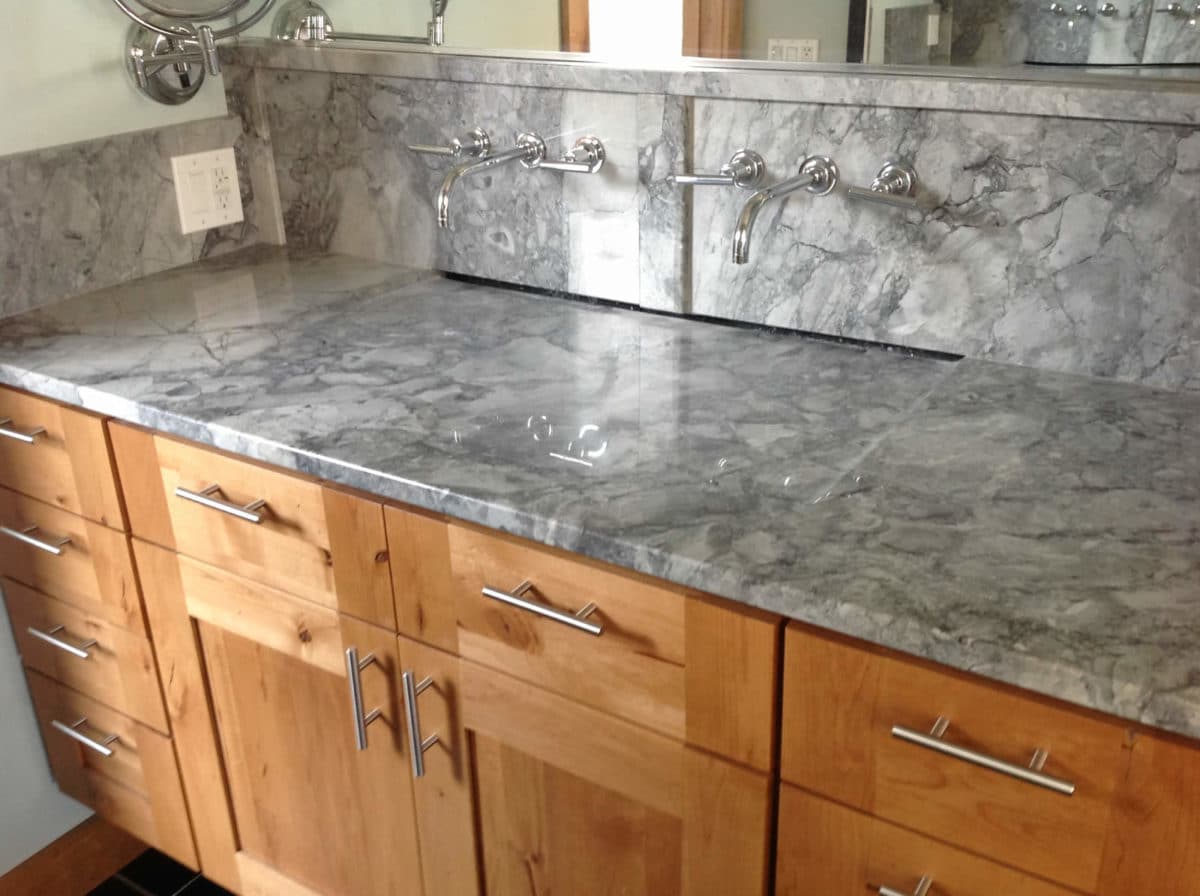 Gray natural stone bathroom vanity with full-height stone backsplash and wall-mount faucets