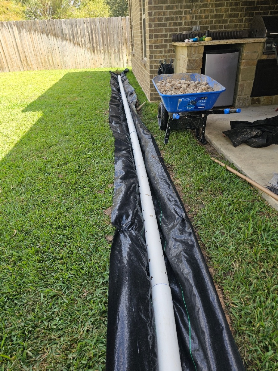 French drain installation in progress on a real Lone Star job, perforated pipe and gravel bed along a home foundation