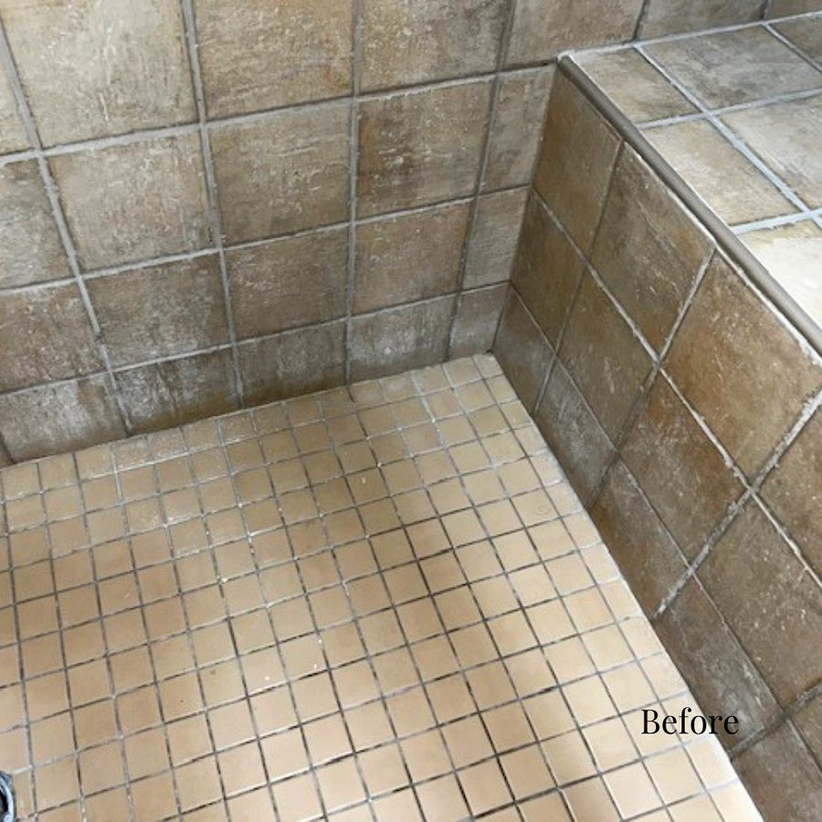 A worn grey tiled shower with a stained bench